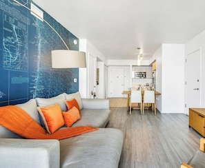 A modern living room with a sofa, a dining area, a kitchen, and a TV displaying 'Avatar: The Way of Water'. - Top-Floor Bay View · 2BR Beachwalk Resort (Hallandale Beach)