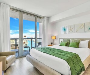 Een hotelkamer met een groot bed, twee bedlampen, uitzicht op de stad en een balkon.