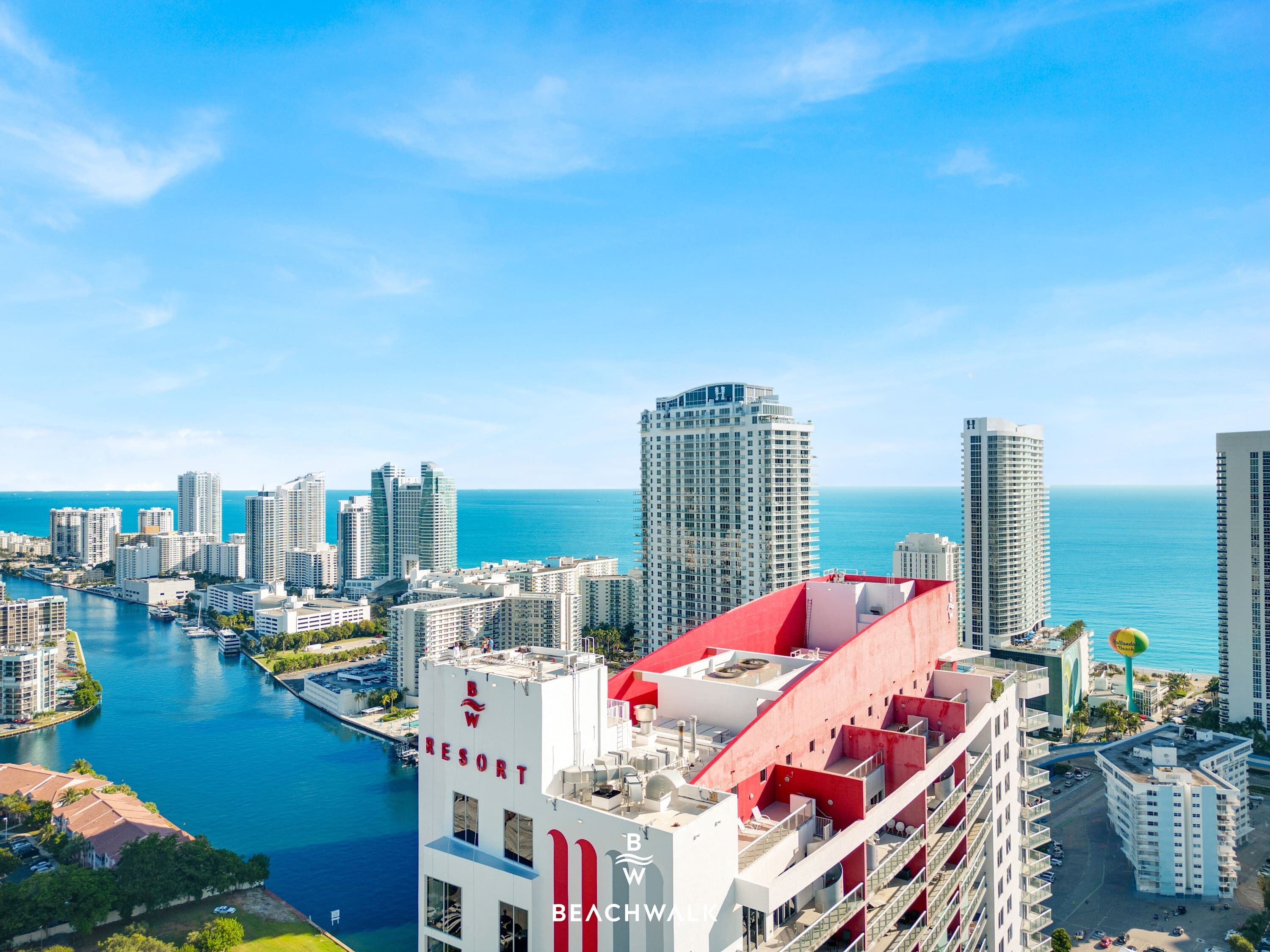 Un edificio alto con techo rojo, que muestra la señalización 'Beachwalk Resort', con vista a una marina y al océano.