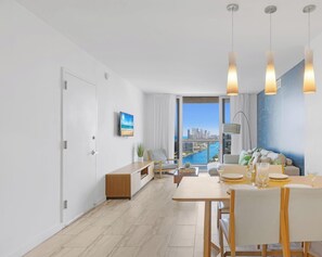 A modern living room with a dining area, large windows with a city view, and a minimalist decor. - Elevated Waterway 2BR · Beachwalk Resort (Hallandale Beach)