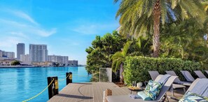 A waterfront balcony with lounge chairs, a pool, and a city skyline in the background. - Elevated Waterway 2BR · Beachwalk Resort (Hallandale Beach)