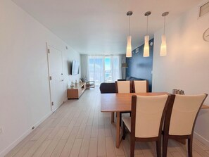 Ein stilvoller Essbereich mit Holztisch und -stühlen, einem an der Wand befestigten Fernseher und Blick auf die Stadt durch das Fenster.