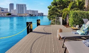 A waterfront balcony with lounge chairs, a pool, and a city skyline in the background. - Intracoastal Living · 2BR Pininfarina Resort (Hallandale Beach)