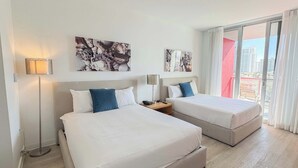 A hotel room with two beds, a bedside table, a lamp, and artwork on the wall. - Beach Escape | Beachwalk Resort Studio (Hallandale Beach)