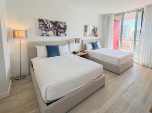 A hotel room with two beds, a bedside table, a lamp, and artwork on the wall. - Beach Escape | Beachwalk Resort Studio (Hallandale Beach)