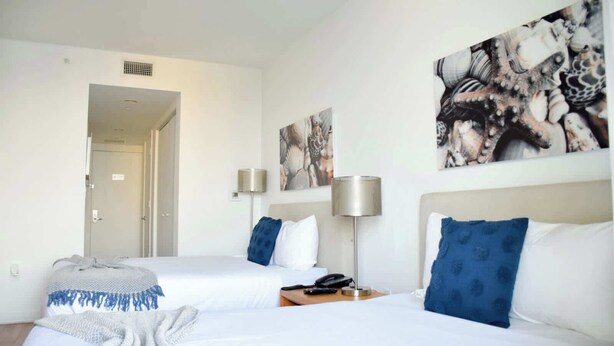 Een hotelkamer met twee bedden, een nachtkastje met een lamp en kunstwerken aan de muren.