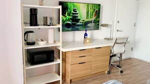 Een moderne kamer met een wit bureau, een magnetron, een koffiezetapparaat, een televisie en een stoel.