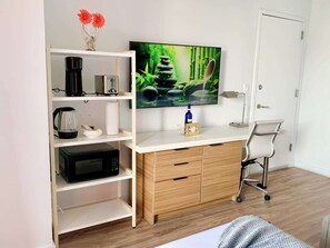 A modern room with a white desk, a microwave, a coffee maker, a TV, and a chair. - Modern Studio w/ Balcony & Intracoastal View (Hallandale Beach)