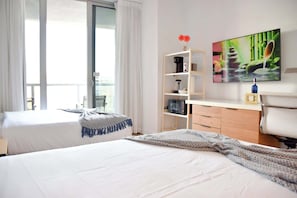 A hotel room with two beds, a wooden dresser, a television, and a window with curtains. - Modern Studio w/ Balcony & Intracoastal View (Hallandale Beach)