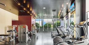 Ein Fitnessraum mit Cardiogeräten, Gewichten und großen Fenstern mit Blick ins Freie.