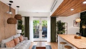 Ein modernes Wohnzimmer mit einer Couch, einem Couchtisch und Barhocker. Ein Schiebetür aus Glas führt zu einem Balkon.