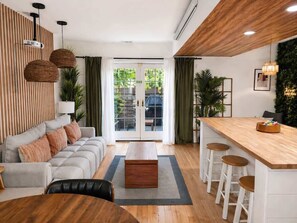 Ein modernes Wohnzimmer mit einer Couch, einem Couchtisch und Barhocker. Ein Schiebetür aus Glas führt zu einem Balkon.
