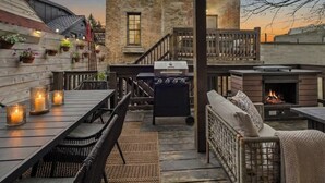 Ein Außenbereich mit Terrasse, Grill, Sitzgelegenheiten und Blick auf ein Backsteinhaus.