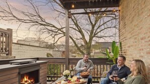 A covered outdoor patio with a fireplace, seating, and a table set for a meal. - Historic Estate | 10 BR, Sleeps 16+, Game Room (Chicago)