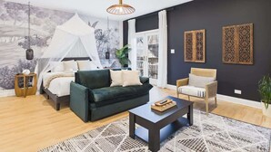 A modern living room with a bed, a green sofa, a wooden coffee table, and a chair. - Historic Estate | 10 BR, Sleeps 16+, Game Room (Chicago)