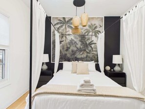 Ein Schlafzimmer mit einem Bett, zwei Nachttischen, einem Himmelbett, einem Wandgemälde und Pendelleuchten.