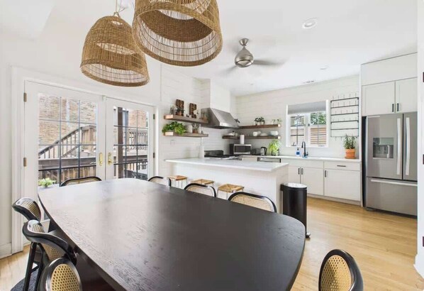 A modern kitchen with white cabinets, a central island, and a dining area with a dark wooden table and wicker chairs. - Historic Estate 10 BR, Game Room, Deck (Chicago)