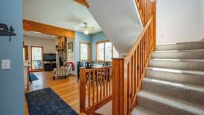 Una escalera con barandillas de madera que conduce a un segundo piso, un comedor con mesa y sillas, y una sala de estar con chimenea.