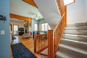 Eine Treppe mit Holzwangen führt zu einer zweiten Etage, ein Essbereich mit Tisch und Stühlen sowie ein Wohnzimmer mit Kamin.