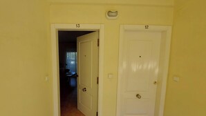 Un pasillo con puertas numeradas 12 y 13, un interruptor de luz y una lámpara fijada a la pared.