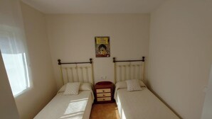 Una habitación pequeña y sencilla con dos camas individuales, una mesita de noche y un póster en la pared.