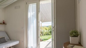 A room with a bed, a sliding glass door to a garden, a small table with a plant, and a book.