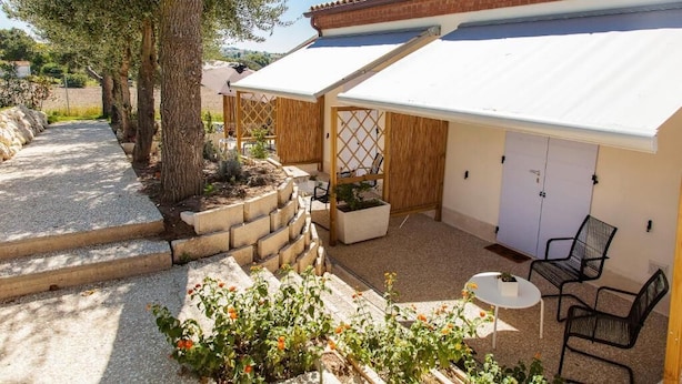 A covered outdoor patio with a table and chairs, a wooden fence, and a building with a tiled roof.