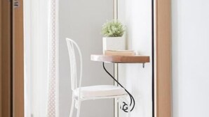 A white chair in a hallway with a wooden shelf holding a plant.