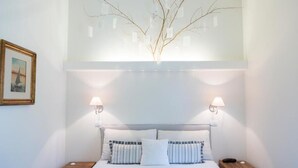 A neatly arranged bedroom with a bed, two bedside tables, a wall-mounted lamp, and a framed picture.