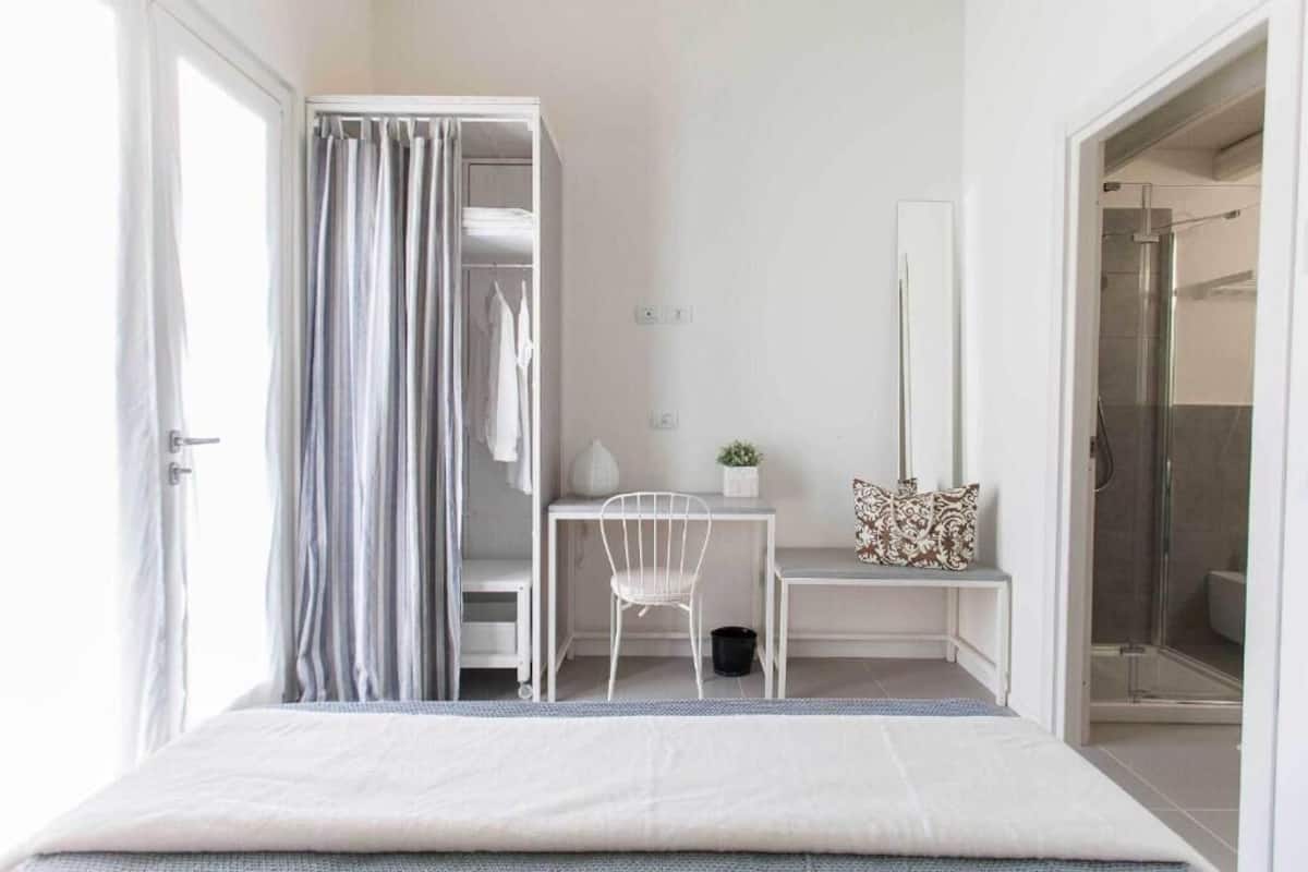 A bedroom with a bed, a desk, a chair, a closet, and a shower.