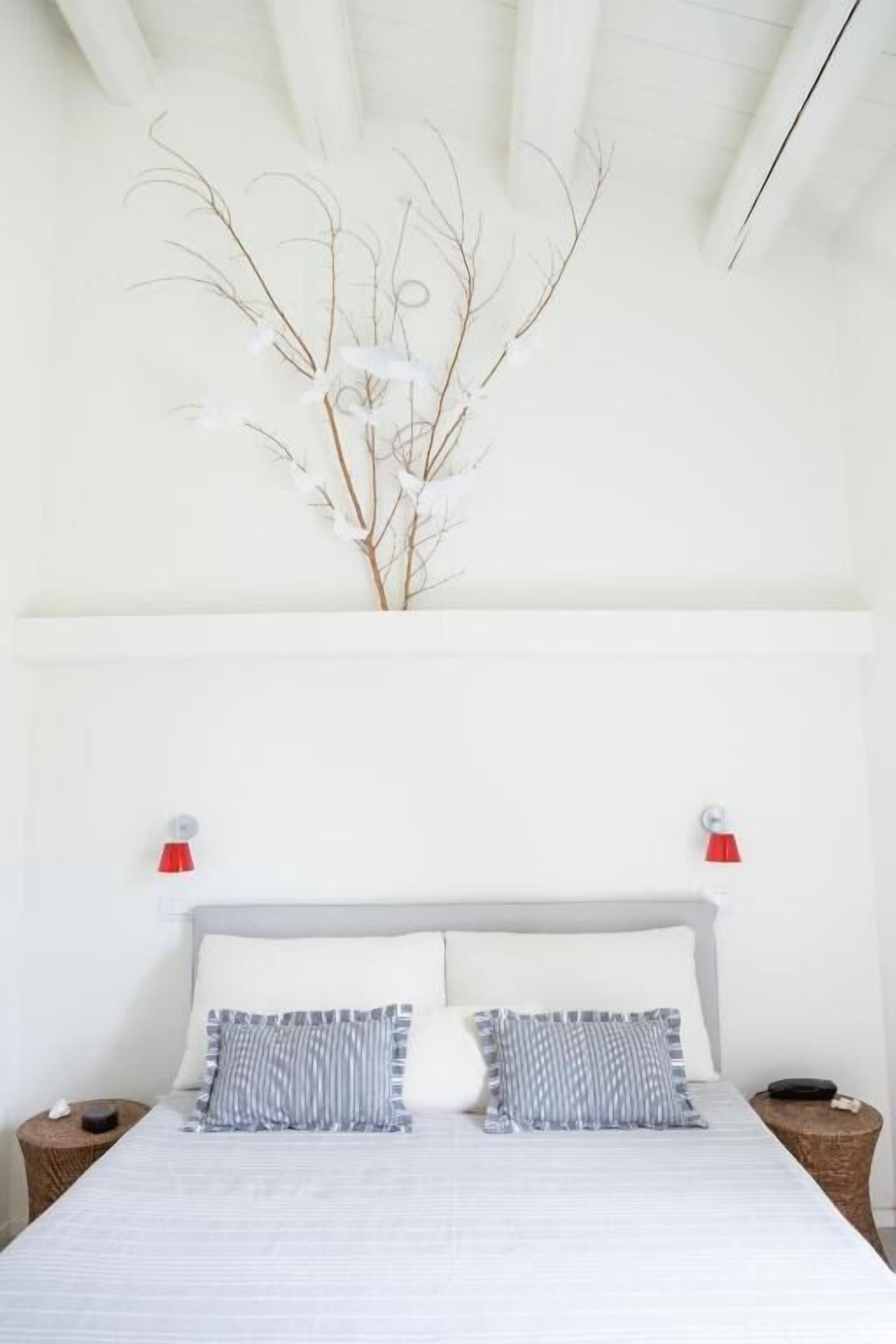 A bed with two pillows, a bedside table, a lamp, and a decorative branch on the wall.
