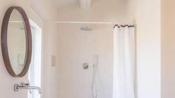 Un baño con tocador de madera, un lavabo grande tipo cuenco, ducha con cortina y un pequeño taburete de madera.