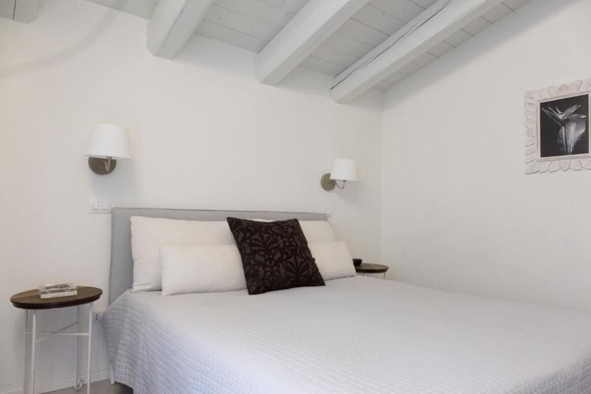 A bedroom with a bed, two bedside tables, a wall-mounted lamp, and a framed picture.