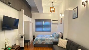 Een moderne slaapkamer met een bed, een bank, een televisie en een ventilator.