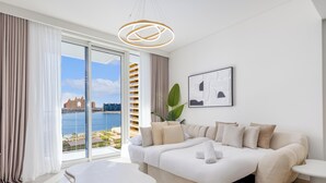 A modern hotel room with a large window, a sofa bed, a bedside table, and a hanging light fixture. - LUX  The Beach Mansion Sea View Suite (Dubai)