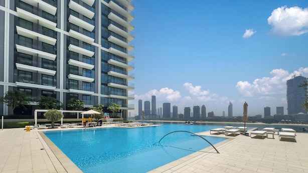 A modern building with a pool area, including lounge chairs and a view of the city skyline. - LUX  The Beach Mansion Sea View Suite (Dubai)