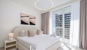A modern hotel bedroom with a large bed, a nightstand, a lamp, and a view of a high-rise building. - LUX  The Beach Mansion Sea View Suite (Dubai)