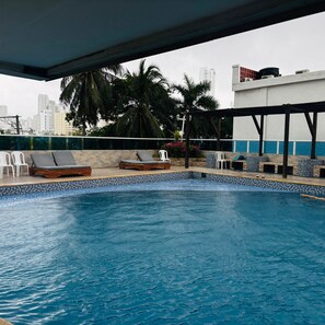 Piscina en la azotea con sillones de descanso y vistas a la ciudad.