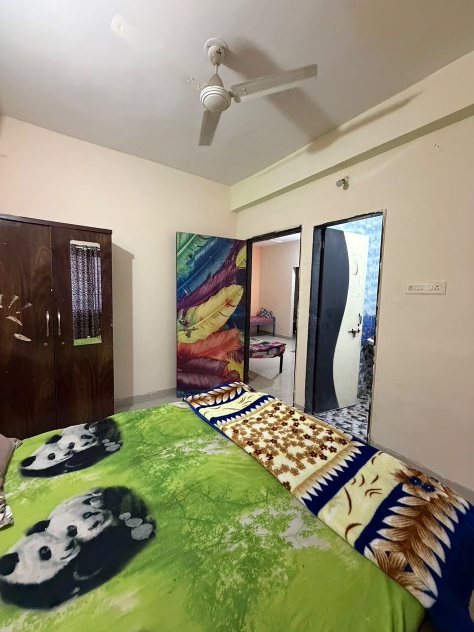 Un dormitorio con cama, armario, ventilador de techo y puerta que da a otra habitación.