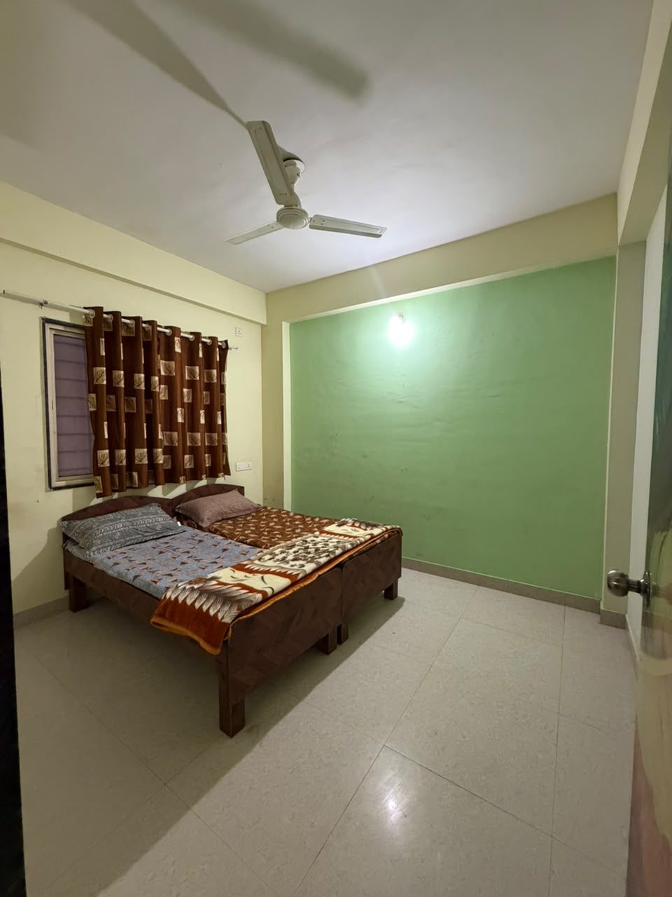 Een slaapkamer met een bed, gordijnen, een plafondventilator en een groene muur.