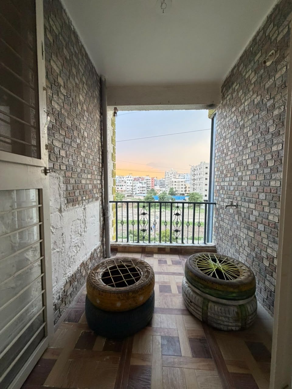 A balcony with a view of buildings, a tiled floor, and two tire planters.