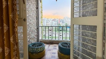 Un balcón con cortinas estampadas, vista panorámica de la ciudad y dos neumáticos grandes como asientos.