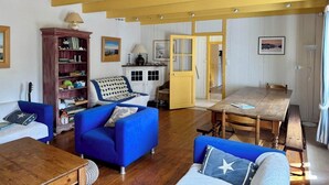 Sala de estar com sofá azul, mesa de centro de madeira, estante e área de jantar com mesa e cadeiras de madeira.