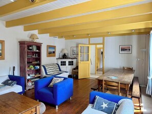 Ein Wohnzimmer mit blauem Sofa, einem Holztisch, einem Bücherregal und einem Essbereich mit Holztisch und Stühlen.