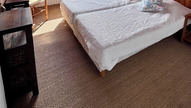 Quarto com teto de madeira, uma cama grande com duas almofadas, uma mesinha, uma cadeira e uma janela com vista para o verde.