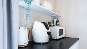 Een kitchenette met een koffiezetapparaat, magnetron en een plank met een fles en andere spullen.