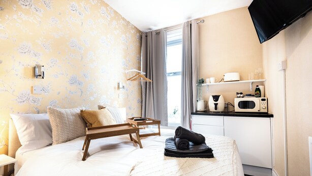 Hotelkamer met een bed, nachtkastje, houten dienblad, opgerolde handdoek, televisie en kitchenette met een magnetron, plus een raam met gordijnen.
