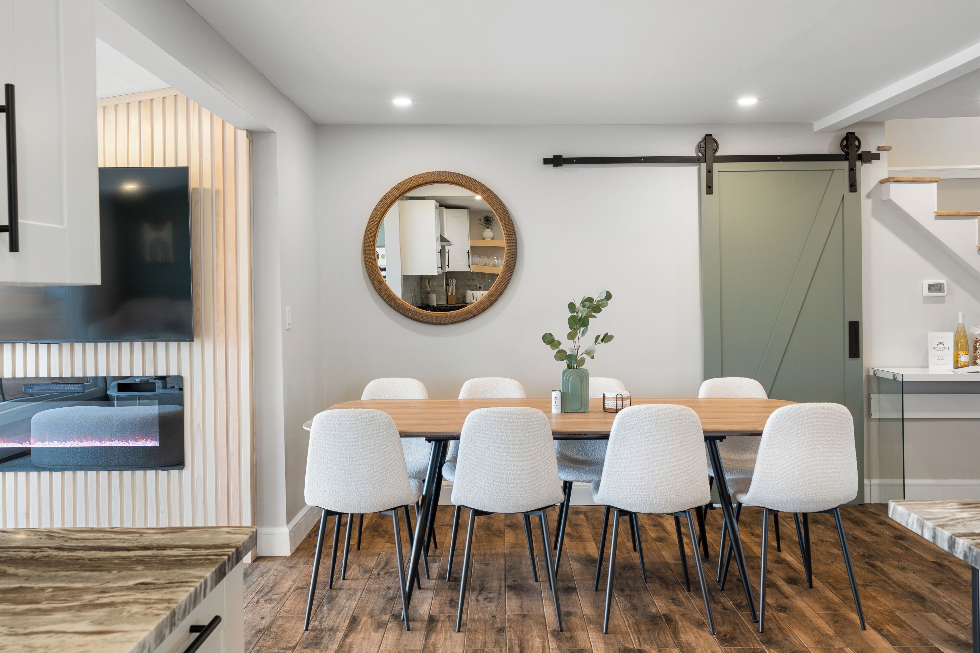 Un comedor moderno con una mesa de madera, seis sillas, un espejo redondo y una puerta corredera.