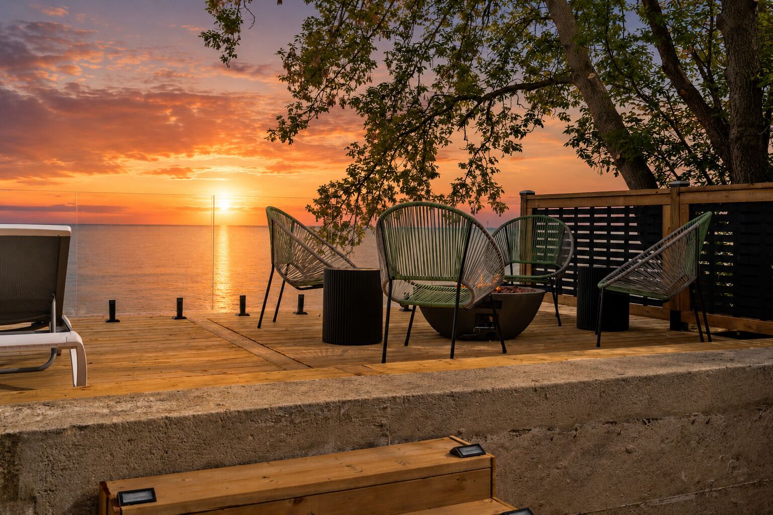 A wooden deck with outdoor seating, a fire pit, and a view of the sunset over the water.