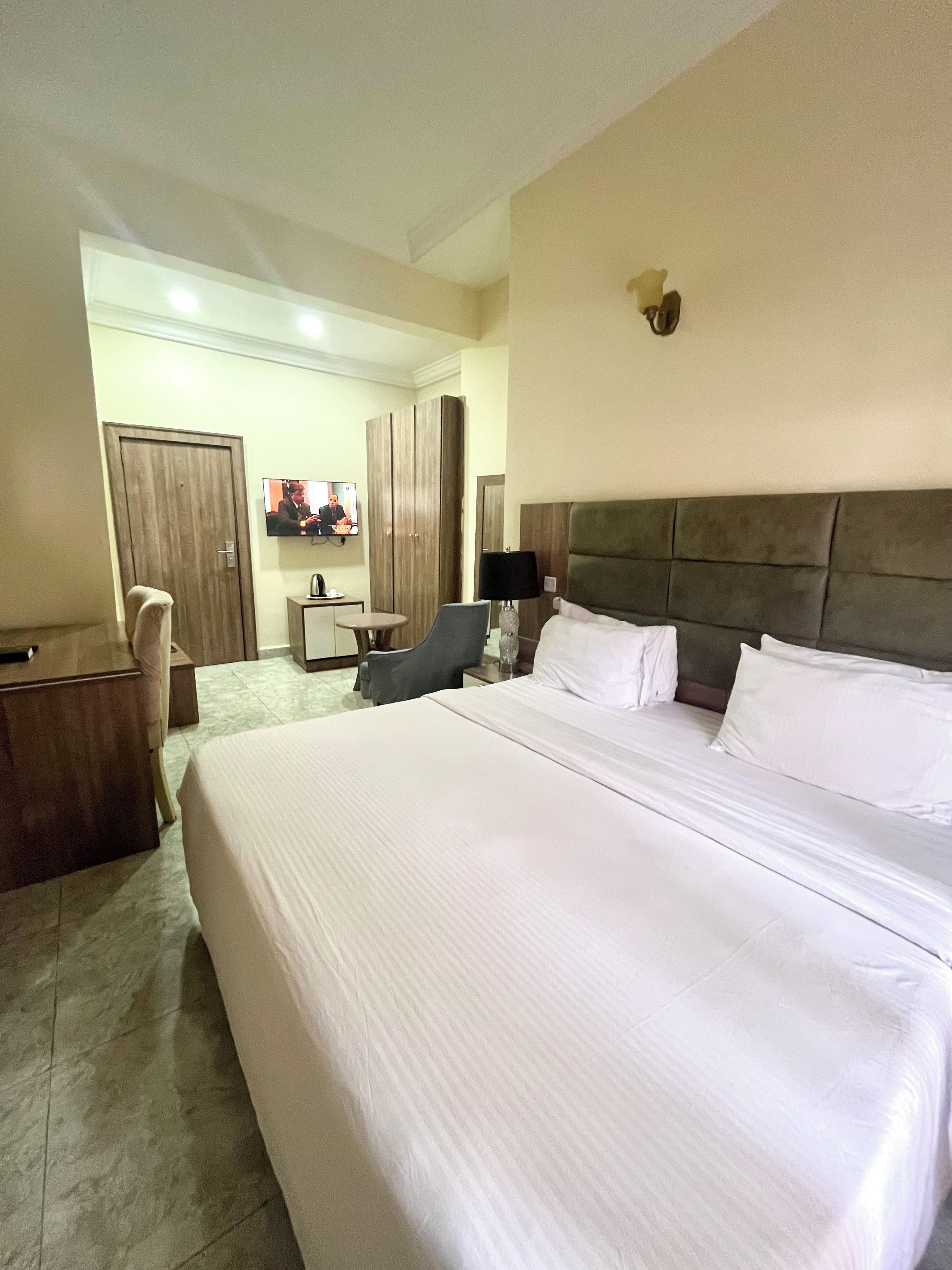 A hotel room with a large bed, a desk, a chair, a television, and a wardrobe.